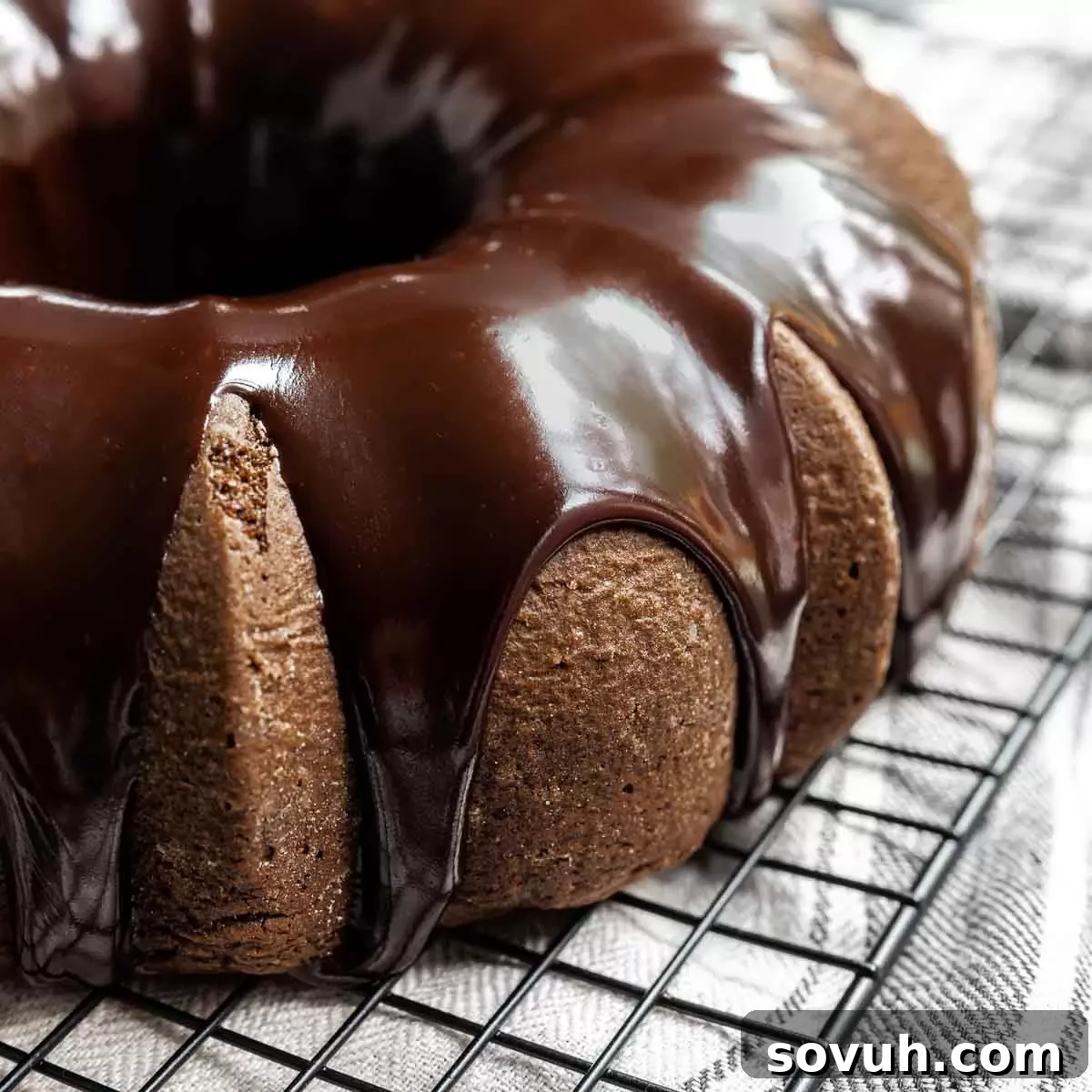 Decadent chocolate fudge cake with a rich ganache glaze cascading down its sides, resting on a serving plate.