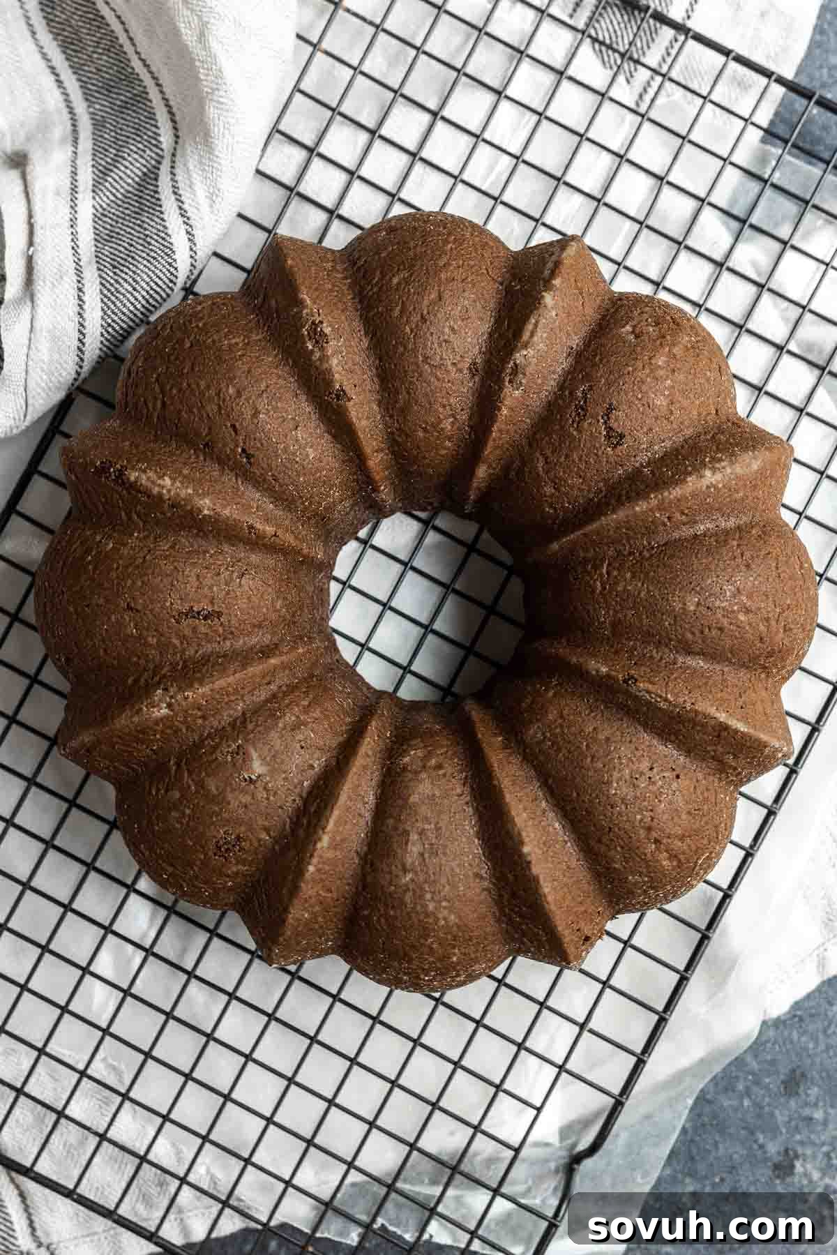 A baked chocolate fudge bundt cake without frosting, resting on a cooling rack, showing its intricate shape.