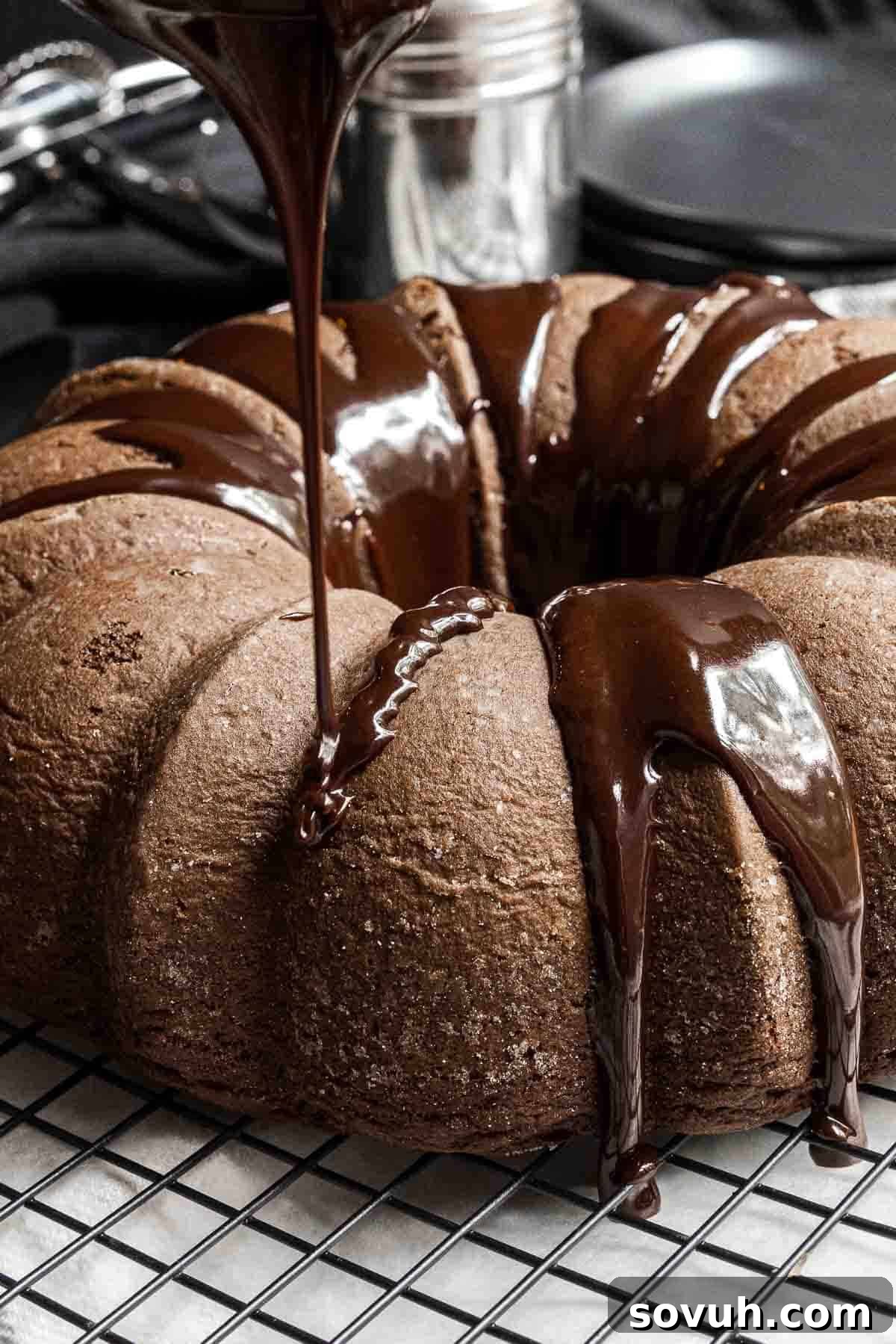 Rich chocolate fudge glaze being poured generously over a perfectly baked chocolate fudge bundt cake on a cooling rack.