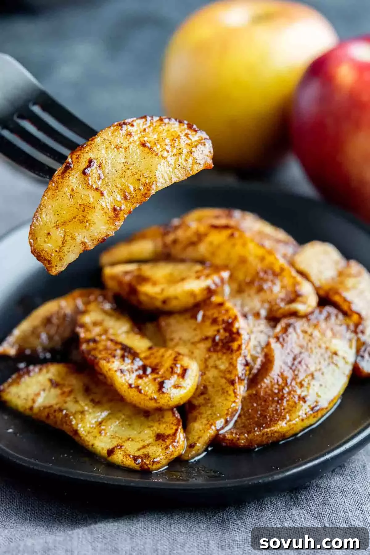Close-up of a single air fryer baked apple slice on a black fork, showing its tender texture and caramelized edges.