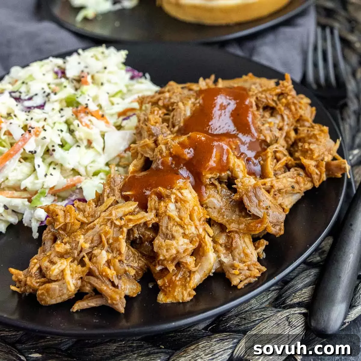 A black plate showcasing Slow Cooker BBQ Pulled Pork alongside a serving of coleslaw, highlighting its delicious appeal.