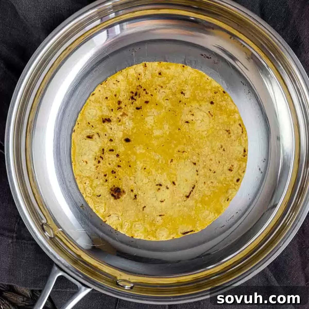 A corn tortilla being lightly toasted in a hot skillet with olive oil.