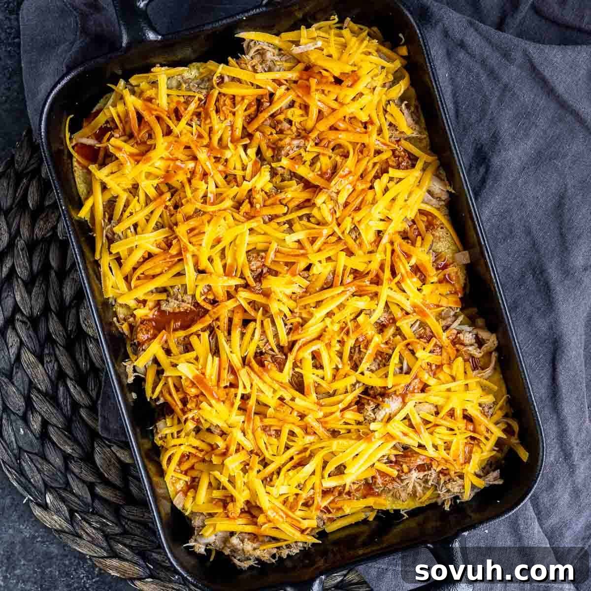 Layering ingredients in a casserole dish: tortillas, pulled pork, enchilada sauce, and cheese.