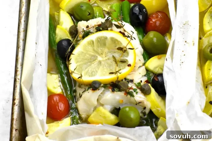 A parchment paper packet with white fish fillet, lemon slices, cherry tomatoes, asparagus, capers, olives, and thyme, ready for baking.