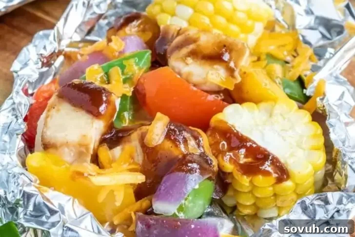 A foil packet containing a mix of grilled vegetables, corn on the cob pieces, and sauced chicken chunks.