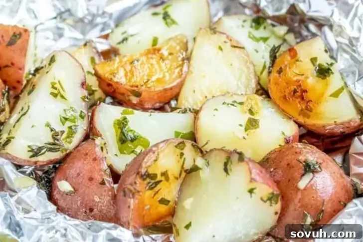 Close-up of roasted potato wedges with herbs in aluminum foil. The potatoes have a golden-brown crust and are garnished with chopped parsley.
