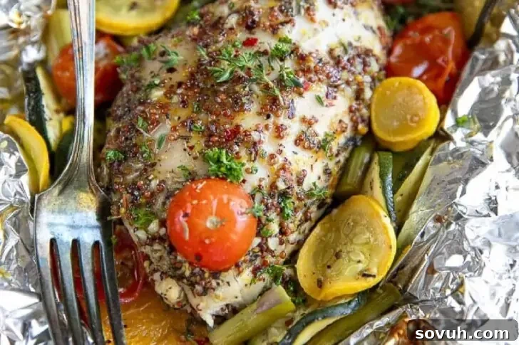 Grilled chicken breast with herbs and quinoa, garnished with cherry tomatoes and sliced zucchini and squash, served on aluminum foil with a fork.