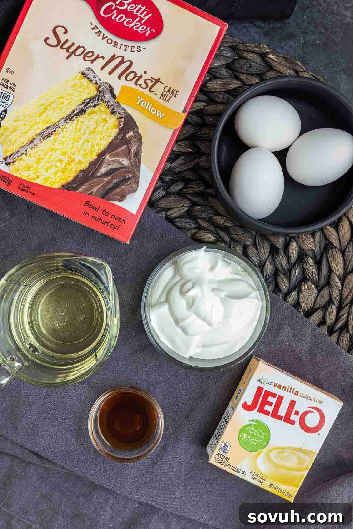 Fresh ingredients laid out for making 4th of July cupcakes in a jar: cake mix, eggs, sour cream, oil, vanilla pudding, heavy cream, powdered sugar, gelatin, vanilla extract, strawberries, and blueberries.