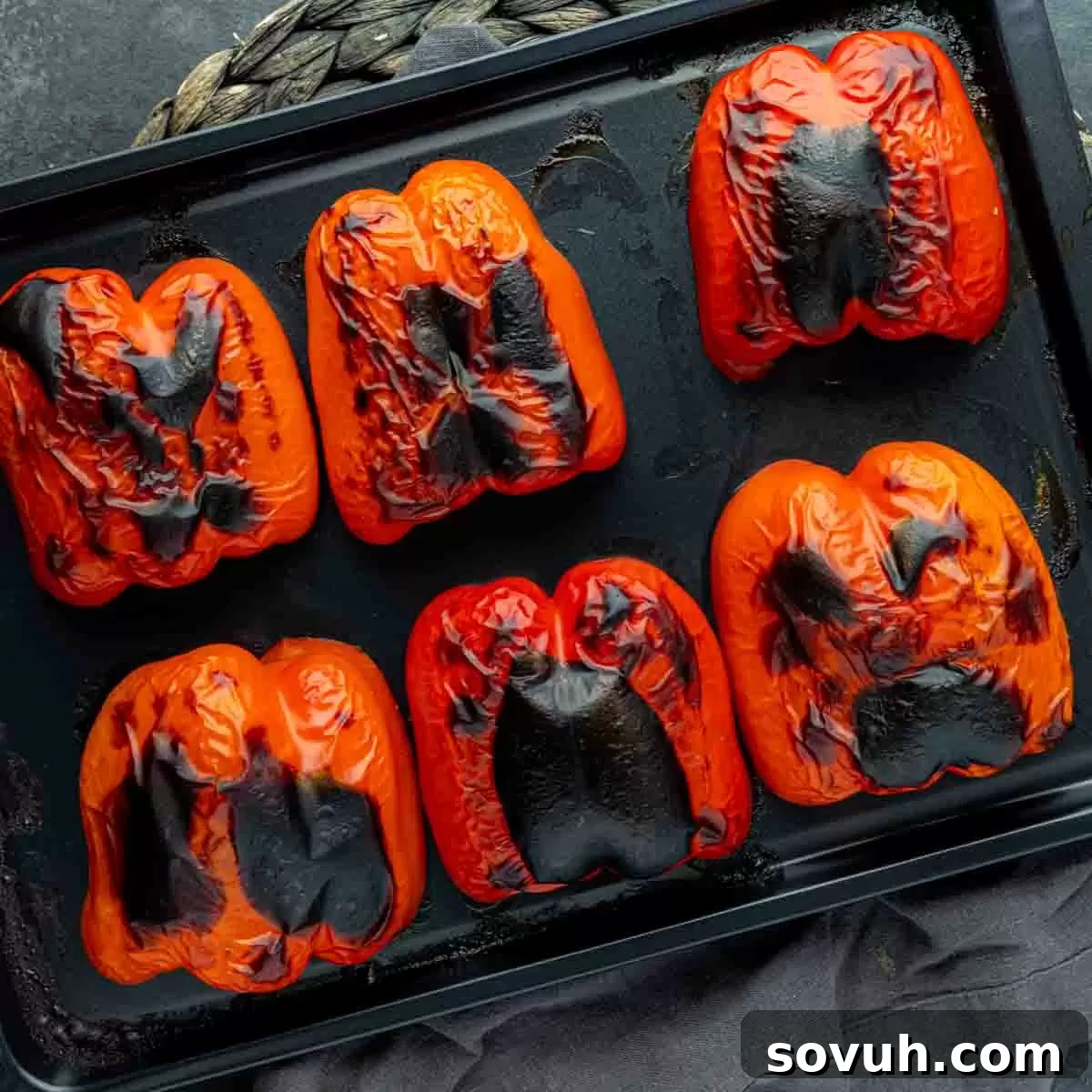 Roasting vibrant red bell peppers on a baking sheet in the oven, emphasizing the process of charring for optimal flavor