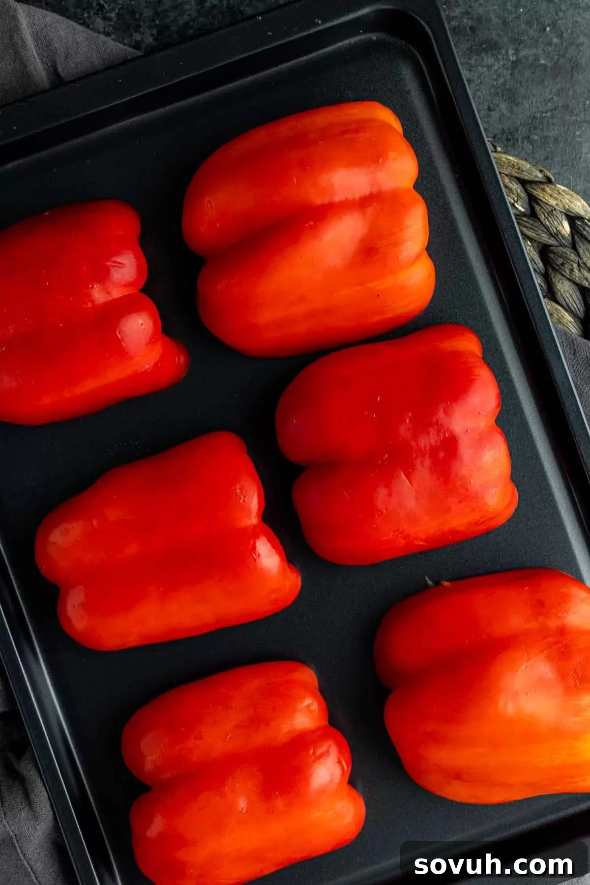 Red bell pepper halves coated in olive oil, arranged skin-side up on a baking sheet, ready to enter the hot oven for roasting