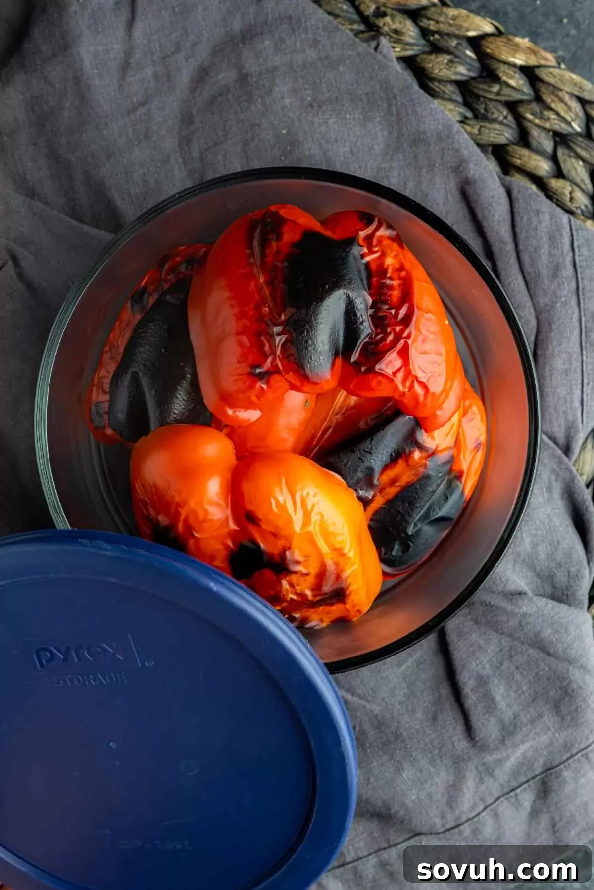 Steaming, freshly roasted red bell peppers placed in a bowl, covered with foil to sweat, a crucial step before peeling the skin