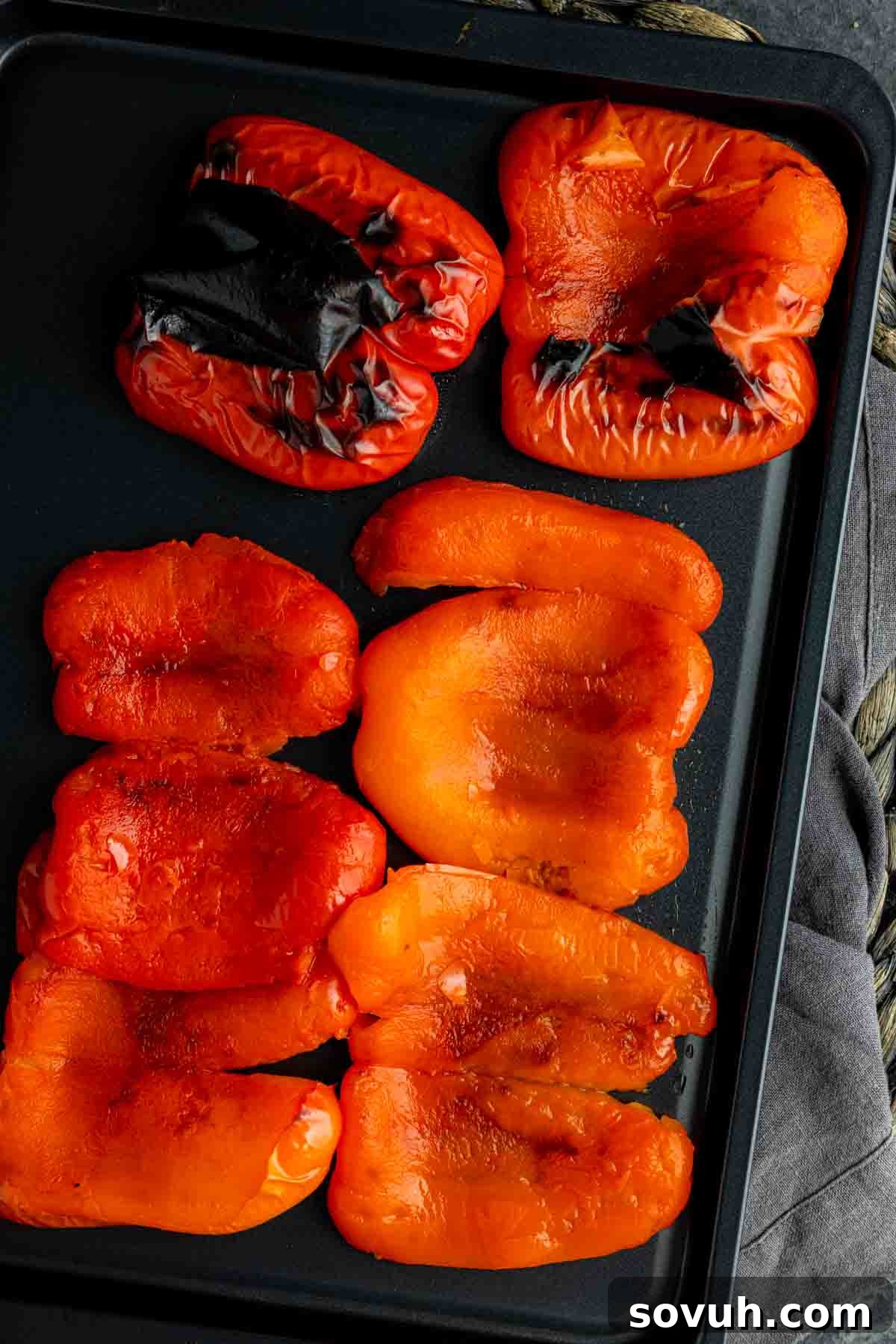 A freshly roasted red bell pepper with perfectly charred skin, cooling on a sheet pan after being removed from the oven