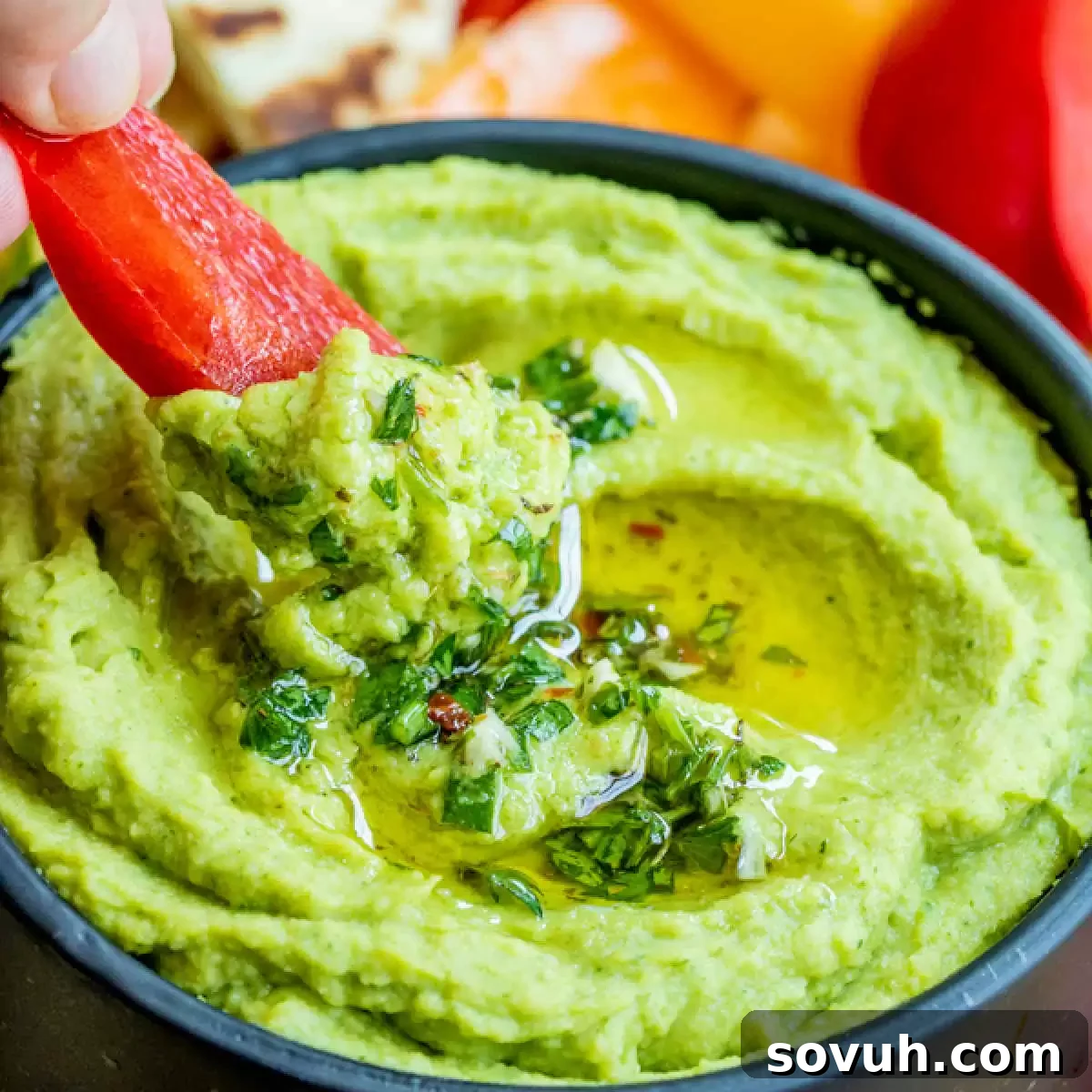 Freshly made Avocado Hummus in a bowl, ready for dipping with vibrant bell peppers.