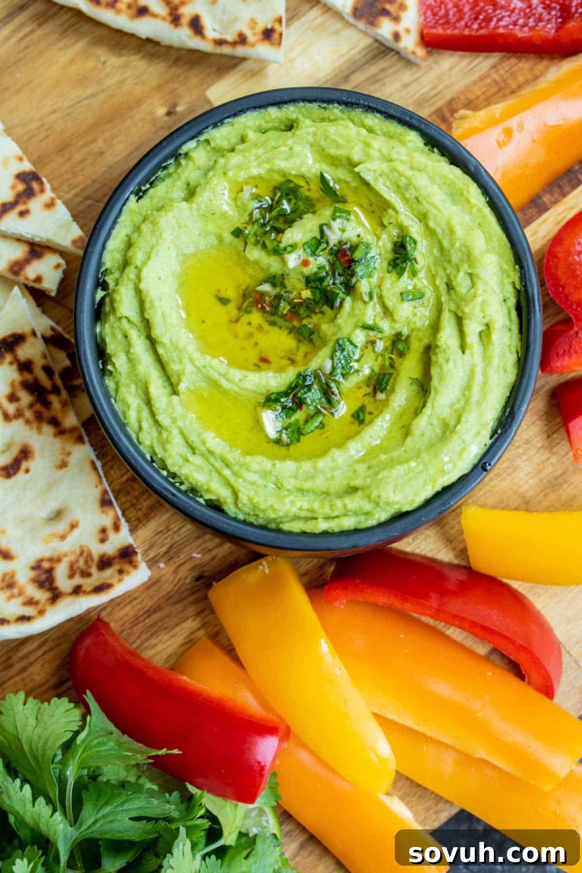 A beautifully arranged serving of Avocado Hummus in a bowl, surrounded by fresh pita bread and colorful bell pepper slices, ready for a healthy snack.