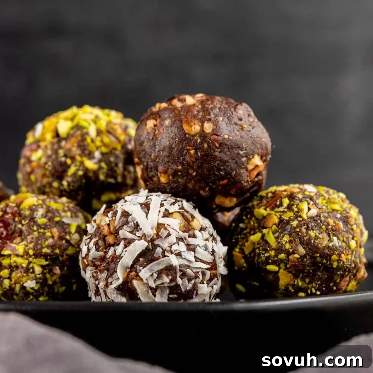 Bliss Balls 2 Delicious chocolate date balls rolled in shredded coconut, artfully arranged on a sleek black plate, highlighting their appetizing texture and presentation.