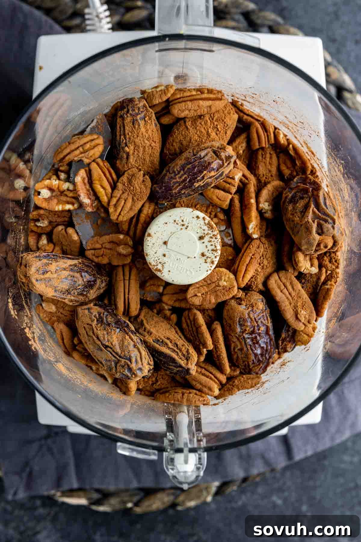 Bliss Balls 4 Dates, pecans, and cocoa powder being combined inside a food processor, poised to be blended into the cohesive mixture for date energy balls.