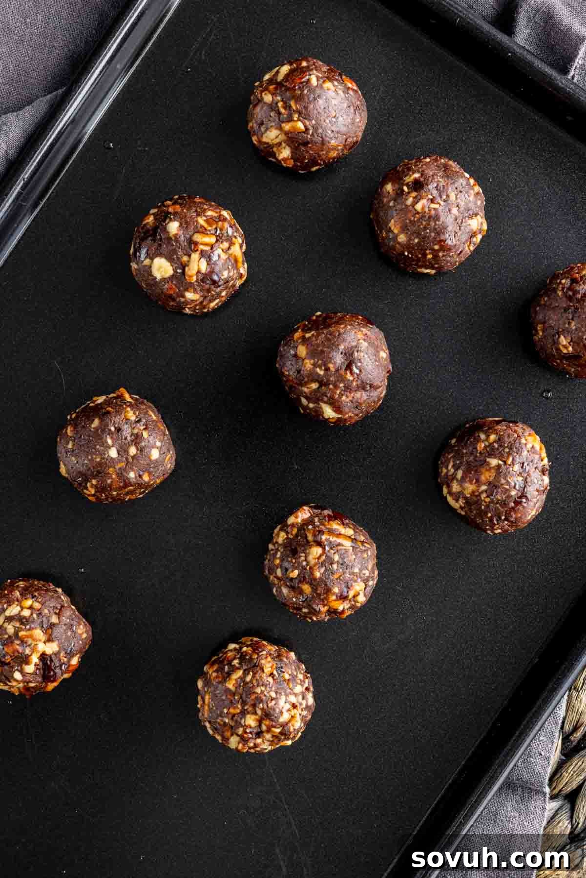 Bliss Balls 6 A collection of freshly rolled chocolate date balls neatly arranged on a black sheet pan, showcasing their uniform size and readiness for chilling or serving.