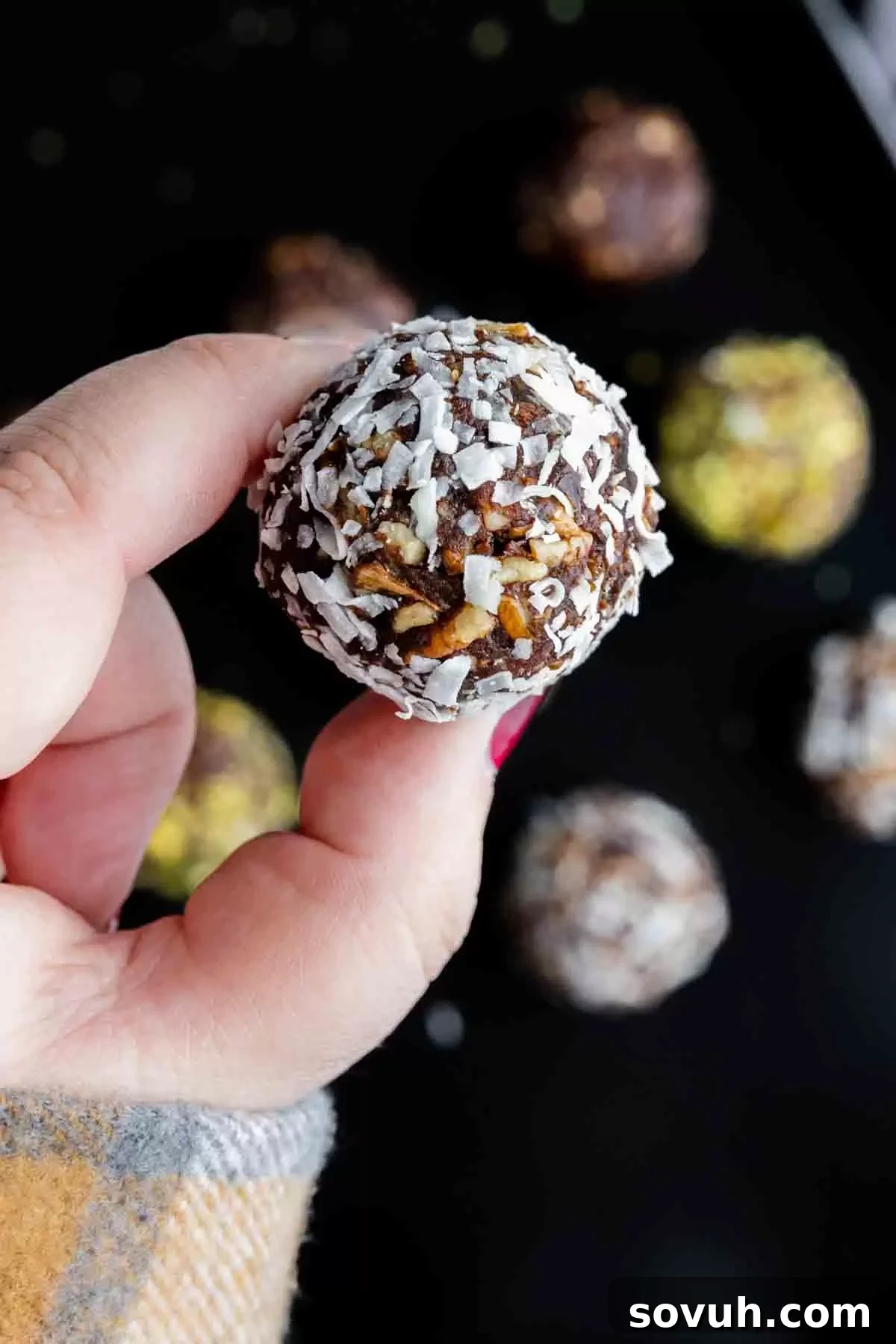 Bliss Balls 8 A hand gently holding a single, perfectly formed date ball coated in shredded coconut, highlighting its size, texture, and readiness for a bite.