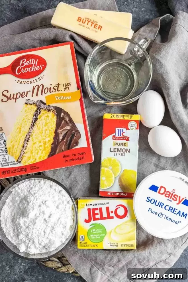 A collection of ingredients laid out for making lemon cupcakes, including cake mix, pudding, sour cream, eggs, oil, butter, powdered sugar, and extracts.