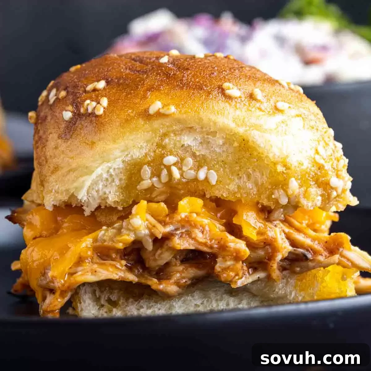 Close-up of delicious baked BBQ chicken sliders on sweet Hawaiian rolls, topped with sesame seeds.
