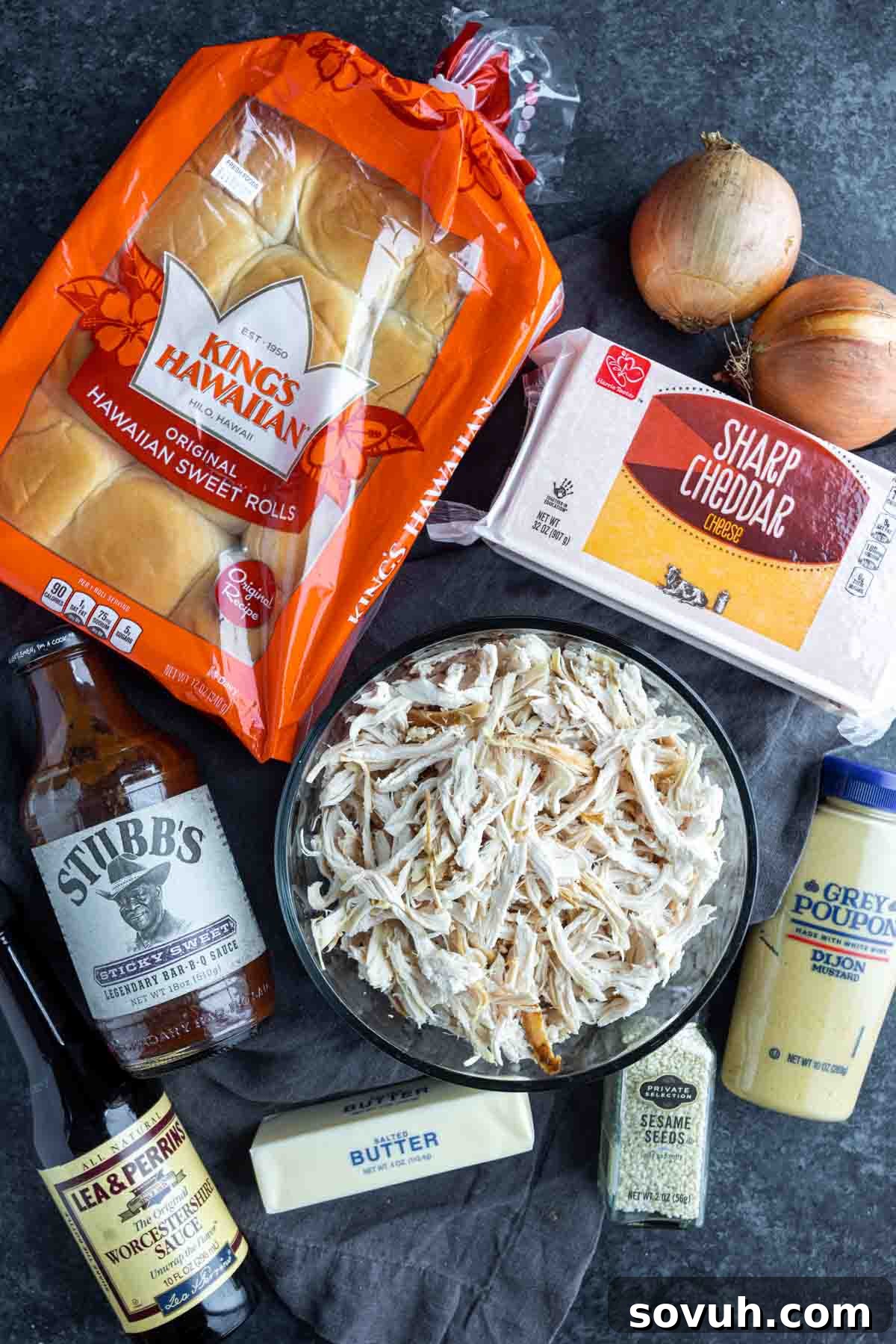 All the fresh ingredients laid out for making BBQ chicken sliders, including buns, shredded chicken, BBQ sauce, cheese, butter, and seasonings.