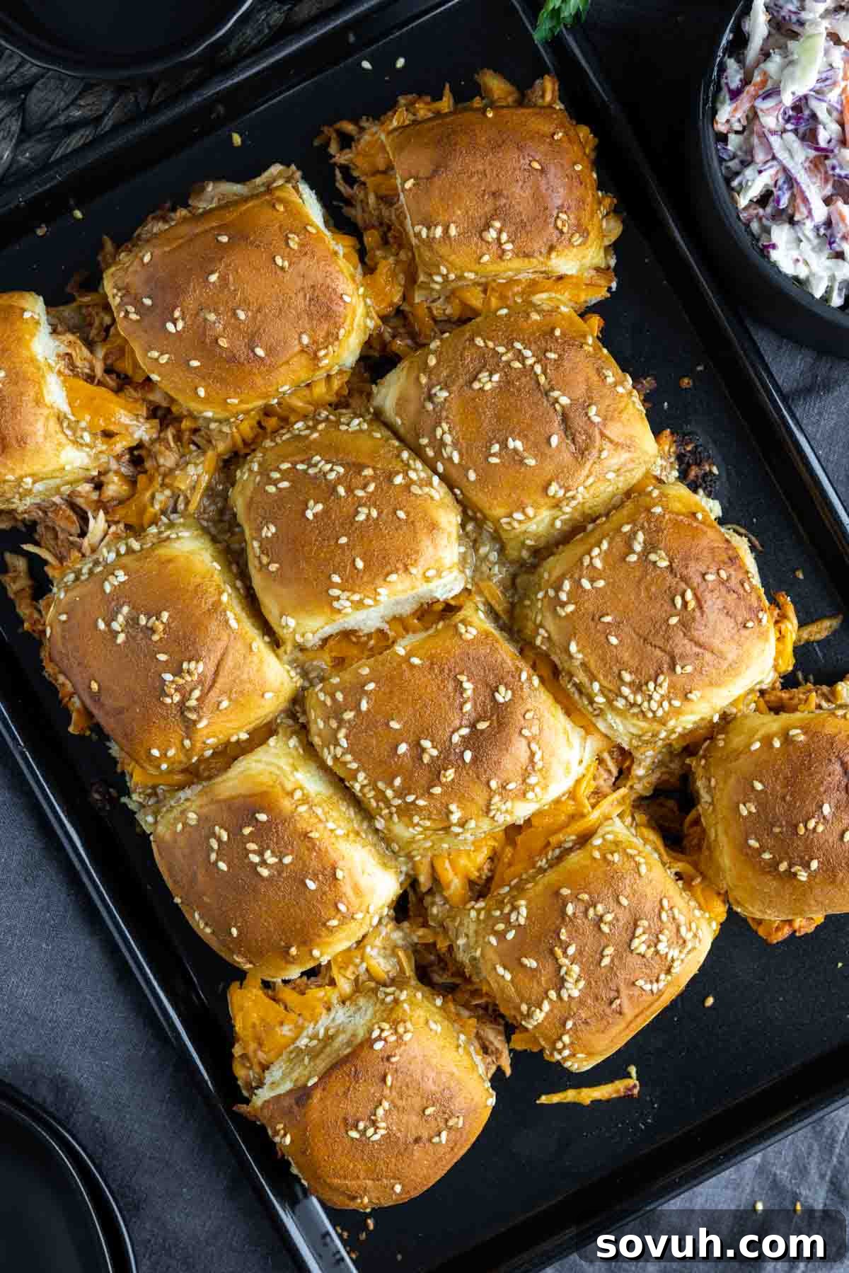 Baked BBQ chicken sliders on a baking sheet, fresh out of the oven, showing melted cheese and toasted buns.