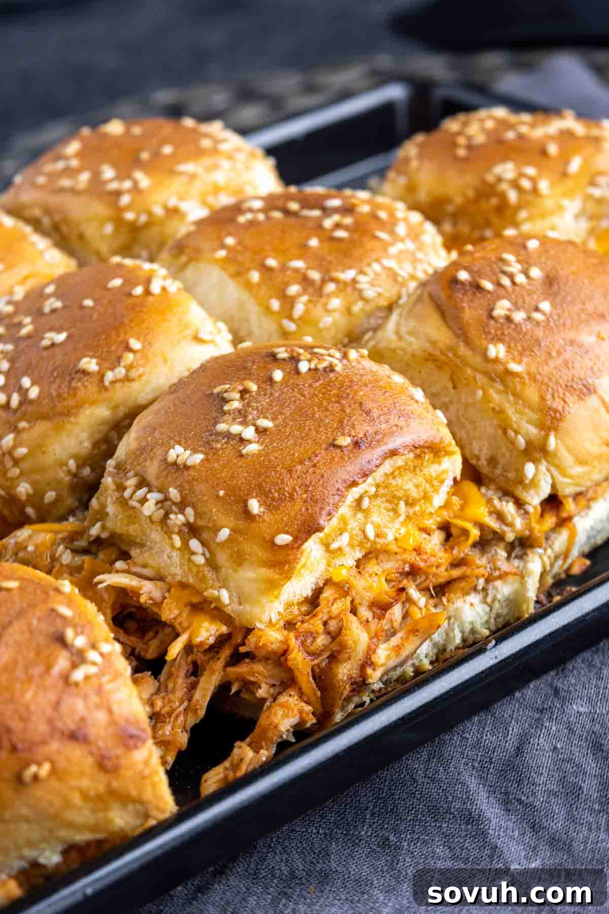 Close-up of perfectly baked BBQ chicken sliders on a baking sheet, showcasing the melted cheese and toasted buns.