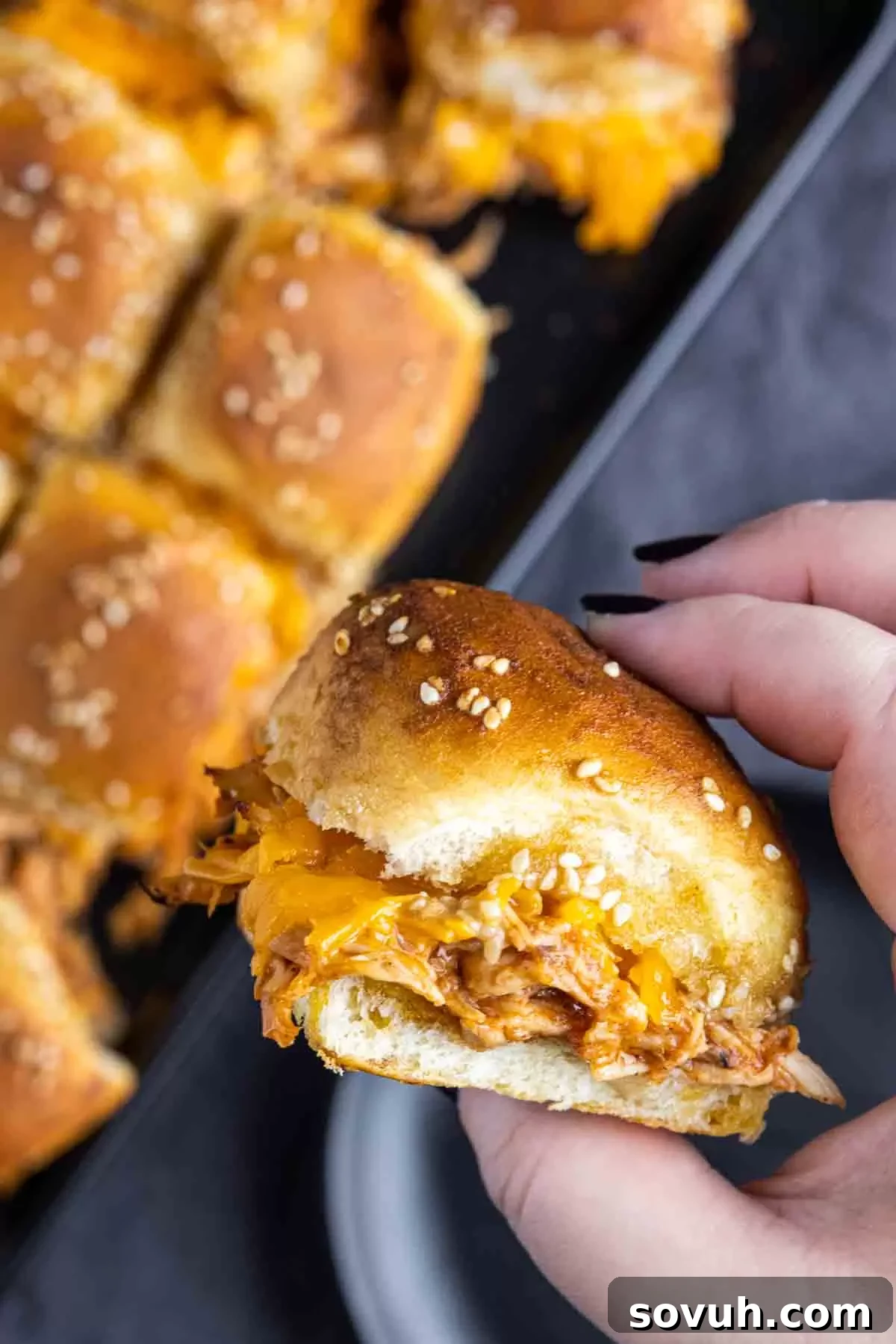 A hand holding a perfectly baked BBQ chicken slider, showcasing its delicious layers and golden bun.