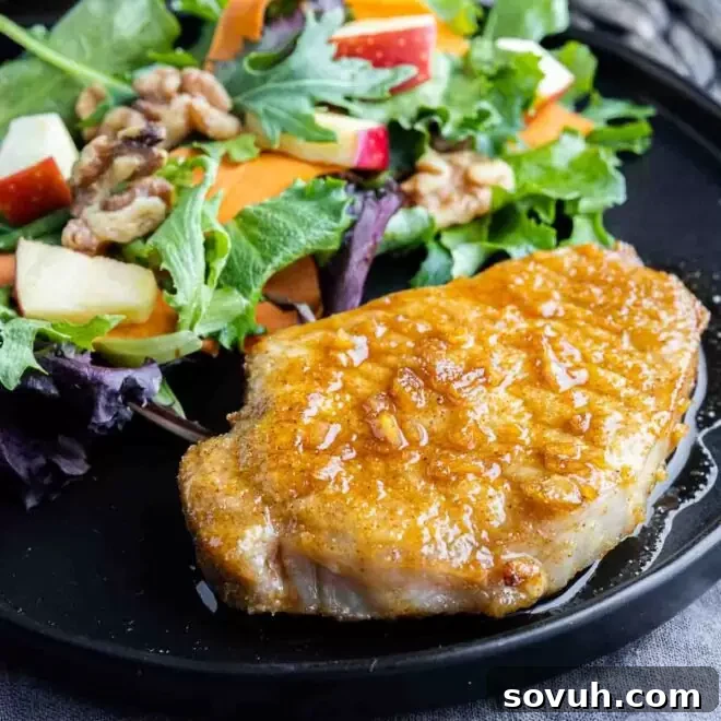 Air Fryer Honey Garlic Pork Chops on a black plate with walnut salad, showing their glistening glaze.