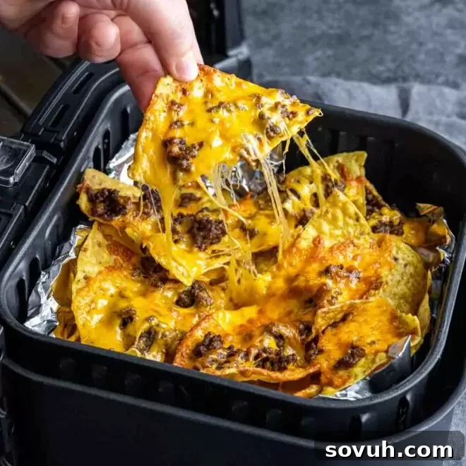 pulling Air Fryer Nachos out of the air fryer, piled high with melted cheese and fresh toppings.