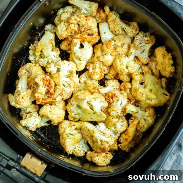 Roasted cauliflower florets in an air fryer basket, showing their golden brown color.