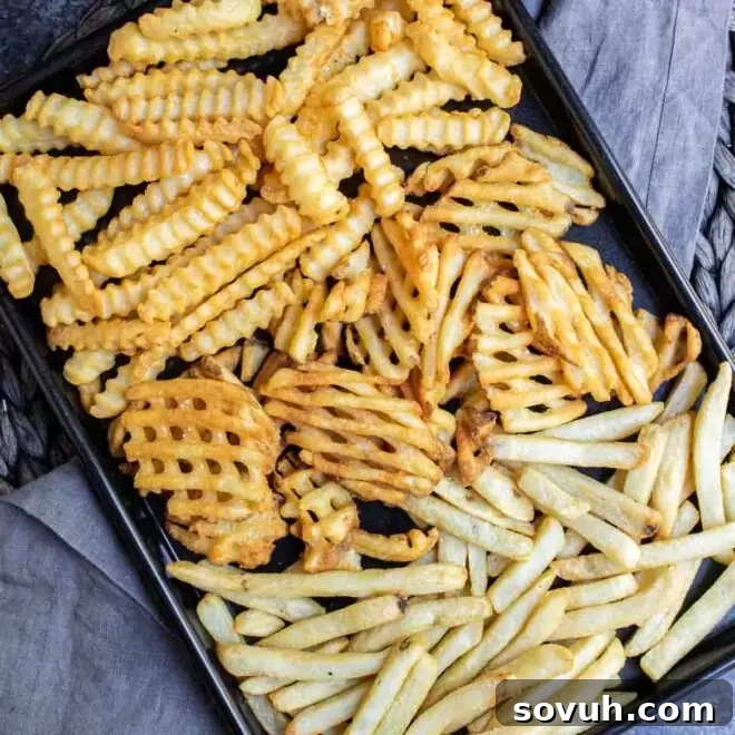 black sheet pan wit Air Fryer Frozen French Fries on gray cloth, golden and ready to eat.