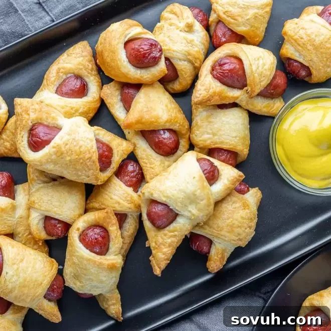 black platter of Air Fryer Pigs in a Blanket with yellow mustard on the side for dipping.