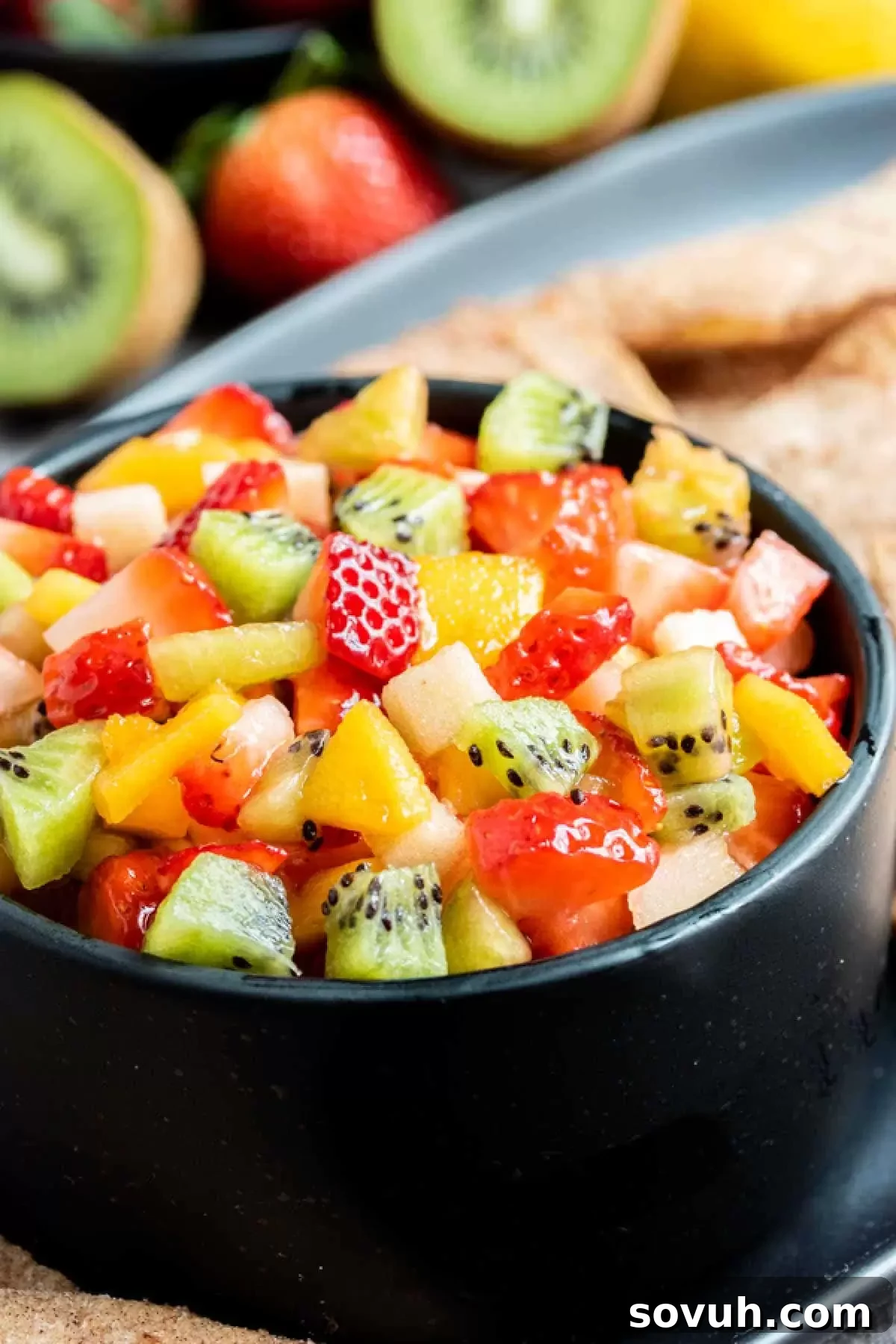 Black bowl filled with colorful fruit salsa, surrounded by whole fruits