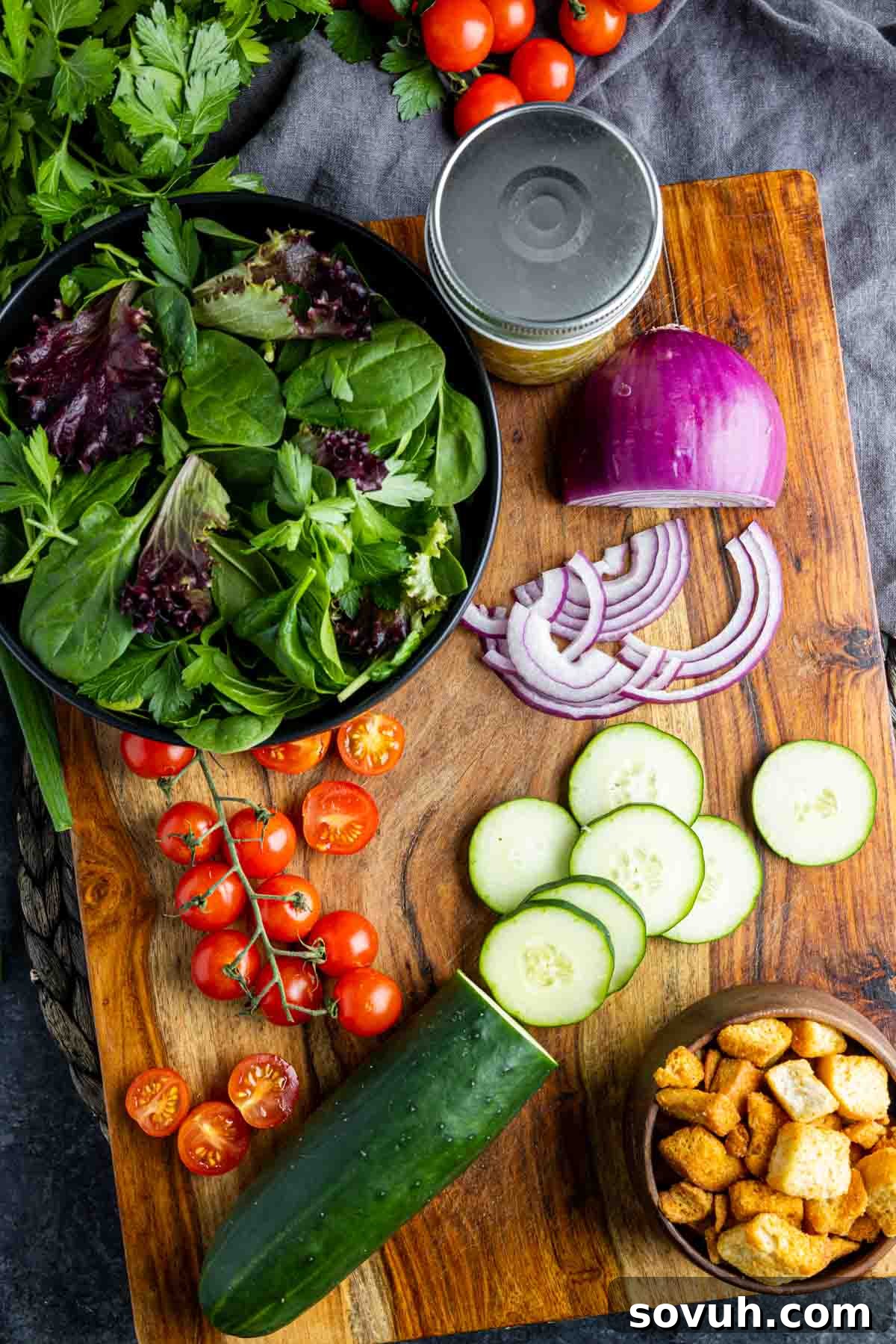 Ingredients for mixed green salad including cucumbers, tomatoes, and various greens arranged appealingly