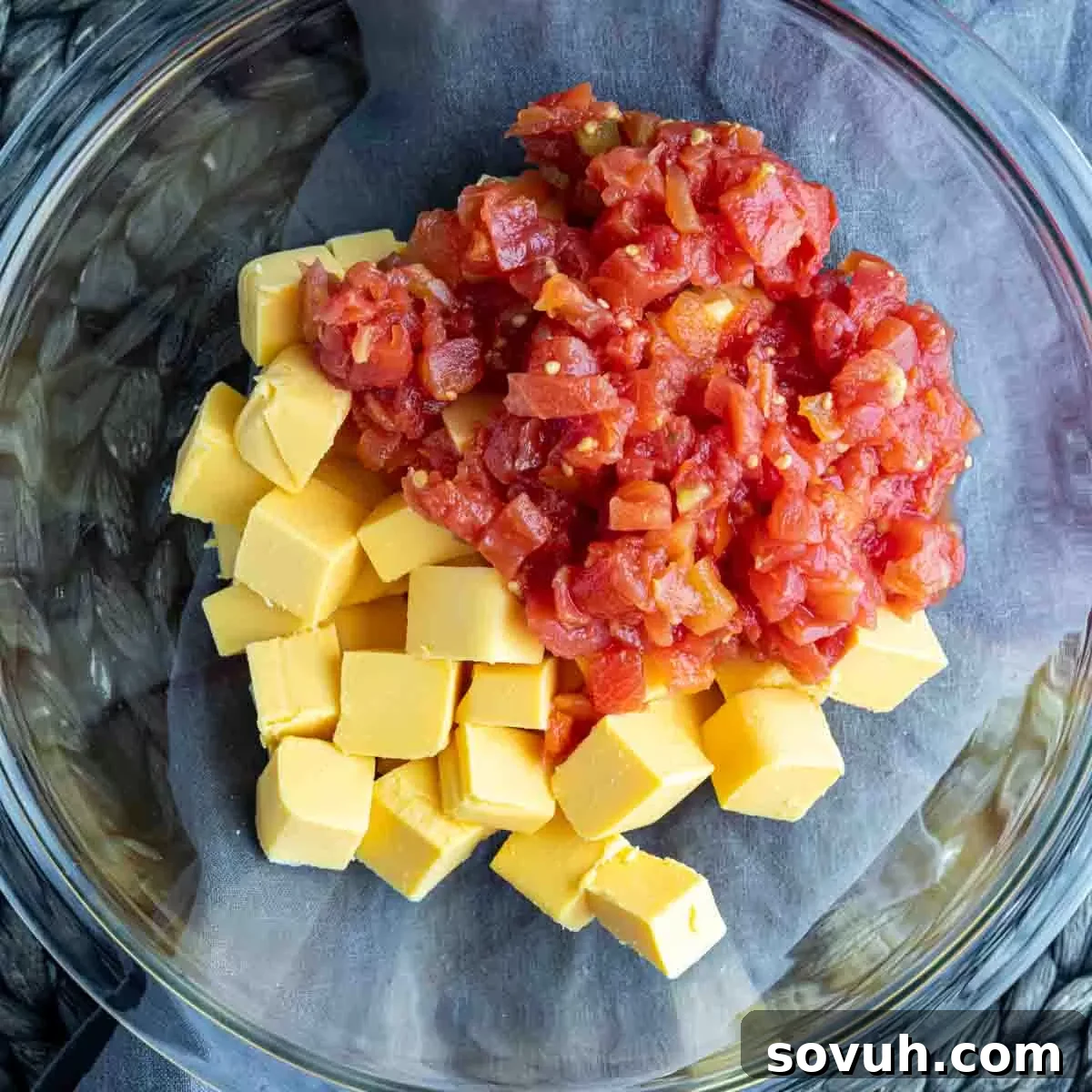 Close-up of cubed Velveeta cheese and a can of Rotel diced tomatoes and green chilies in a glass bowl, ready for microwaving.