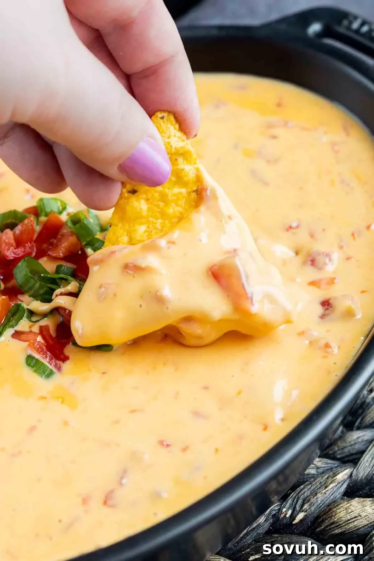 A tortilla chip being dipped into a bowl of warm, creamy Rotel Dip, highlighting its appealing texture.