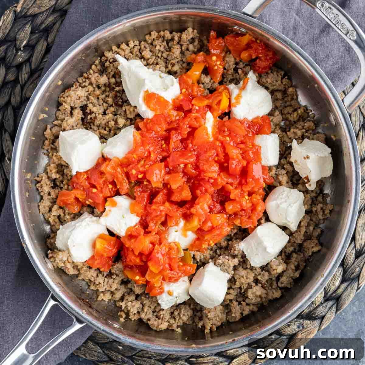 Sausage, cubed cream cheese, and undrained Rotel tomatoes being combined in a skillet.