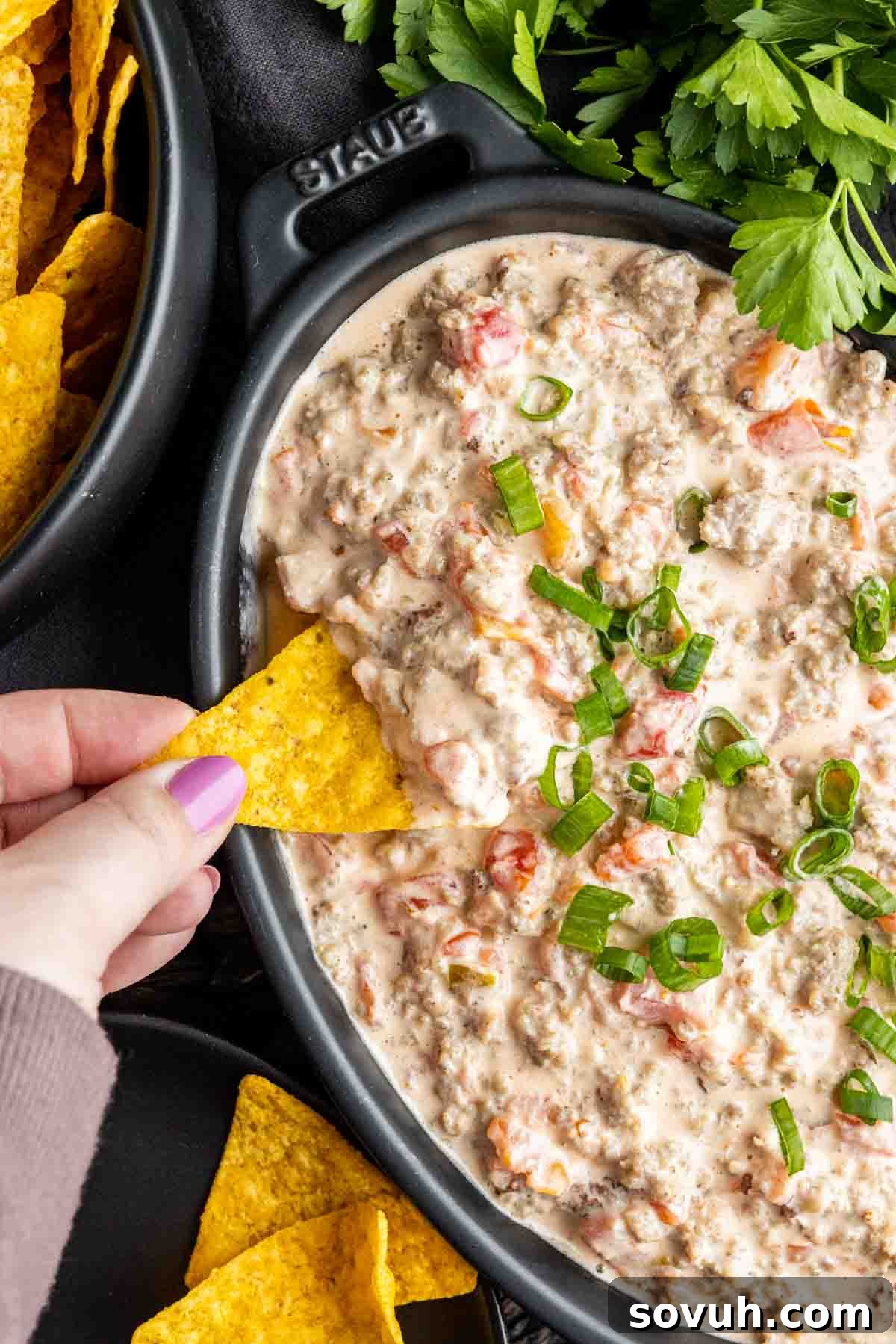 A tortilla chip being dipped into the warm, creamy Sausage Cream Cheese Dip, showcasing its perfect consistency.