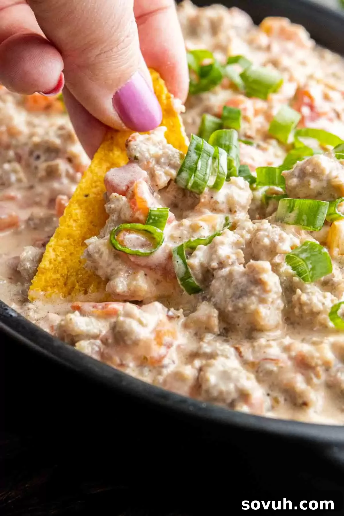 A hand dipping a tortilla chip into the creamy Sausage Cream Cheese Dip, demonstrating its appeal.