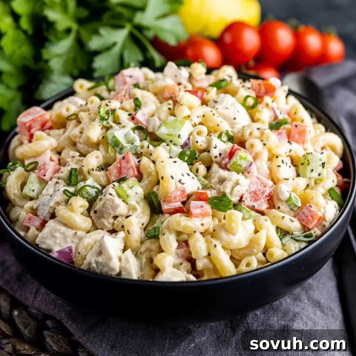Creamy Chicken Macaroni Salad in a black bowl, garnished with fresh parsley and surrounded by ripe cherry tomatoes.