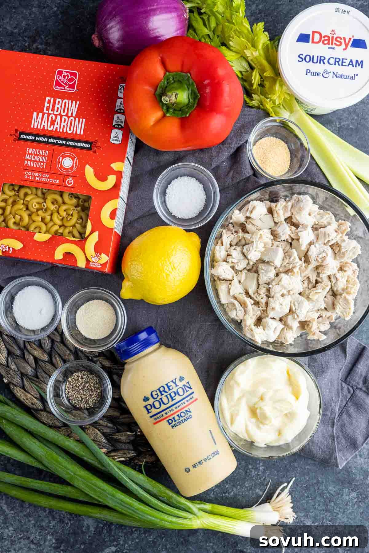 Assorted fresh ingredients for Chicken Macaroni Salad, including cooked macaroni, chopped chicken, and various vegetables in separate bowls.