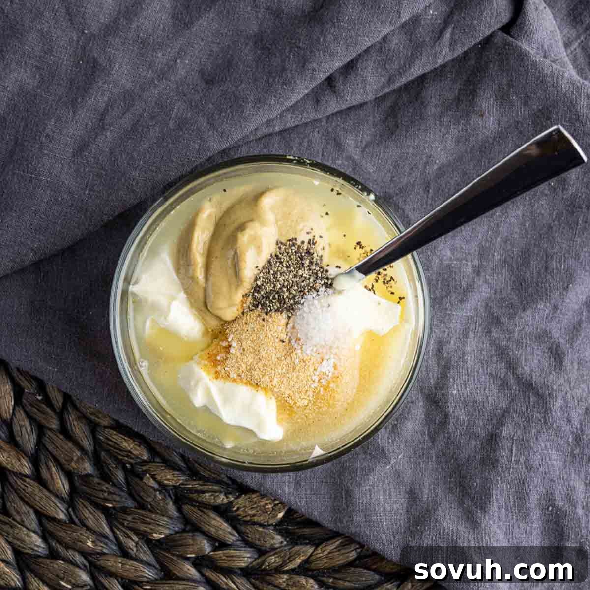 A small glass bowl containing a creamy yellow dressing, made from mayonnaise, sour cream, lemon juice, sugar, Dijon mustard, and spices.