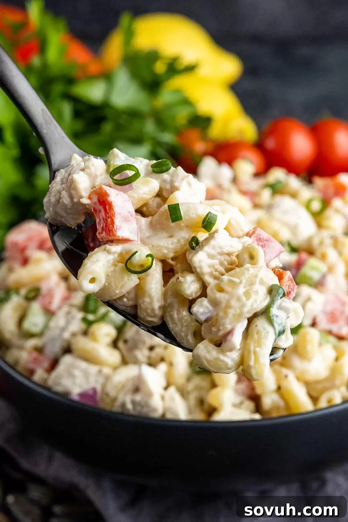 A spoonful of creamy Chicken Macaroni Salad being lifted from a black bowl, showing the texture and ingredients.