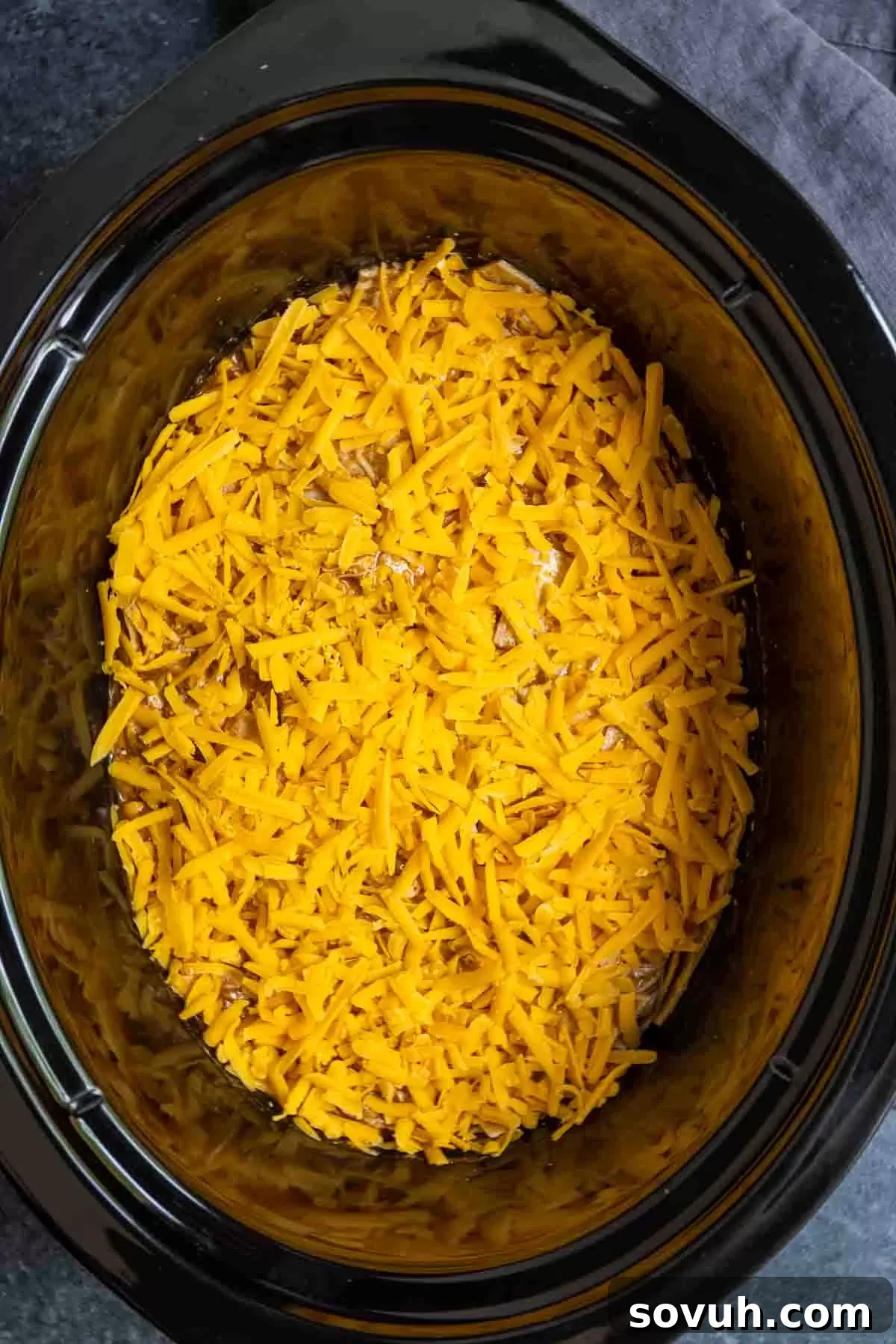 topping Crock Pot Chicken Enchiladas with shredded cheddar cheese