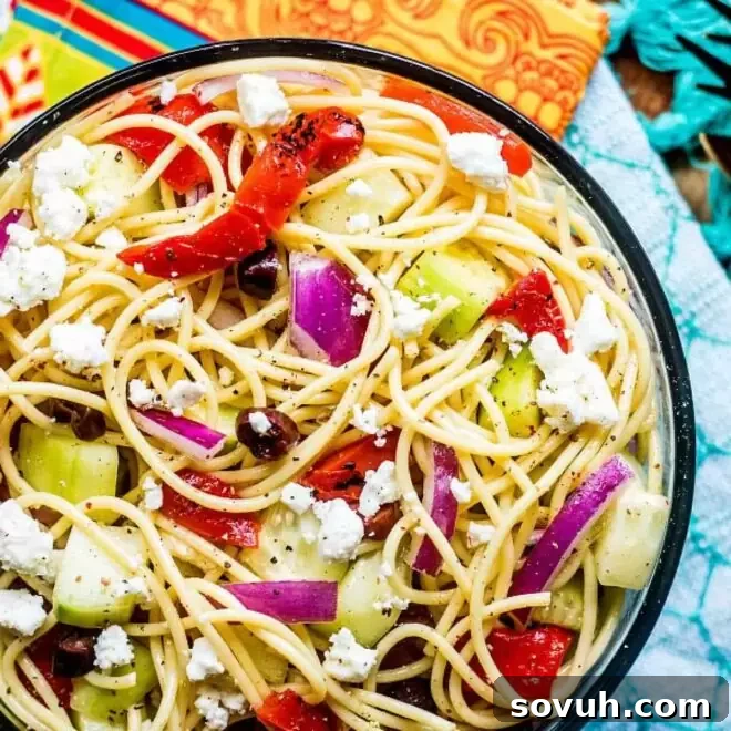 A vibrant glass bowl brimming with fresh and colorful Greek Spaghetti Salad.