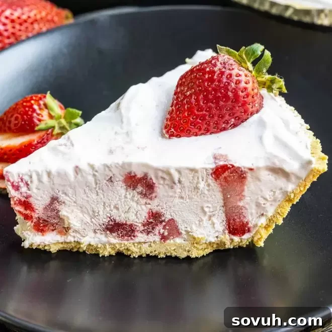 A refreshing slice of Frozen Strawberry Pie served on a black plate, topped with whole fresh strawberries.