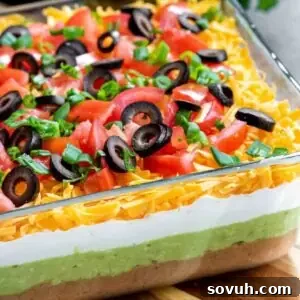 A vibrant, make-ahead Mexican 7 Layer Dip served in a clear glass dish, showcasing its distinct layers of Tex-Mex flavors.