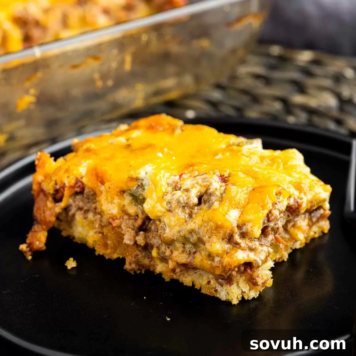 A delicious piece of John Wayne Casserole on a black plate, showcasing its golden cheese topping, creamy filling, and biscuit base.