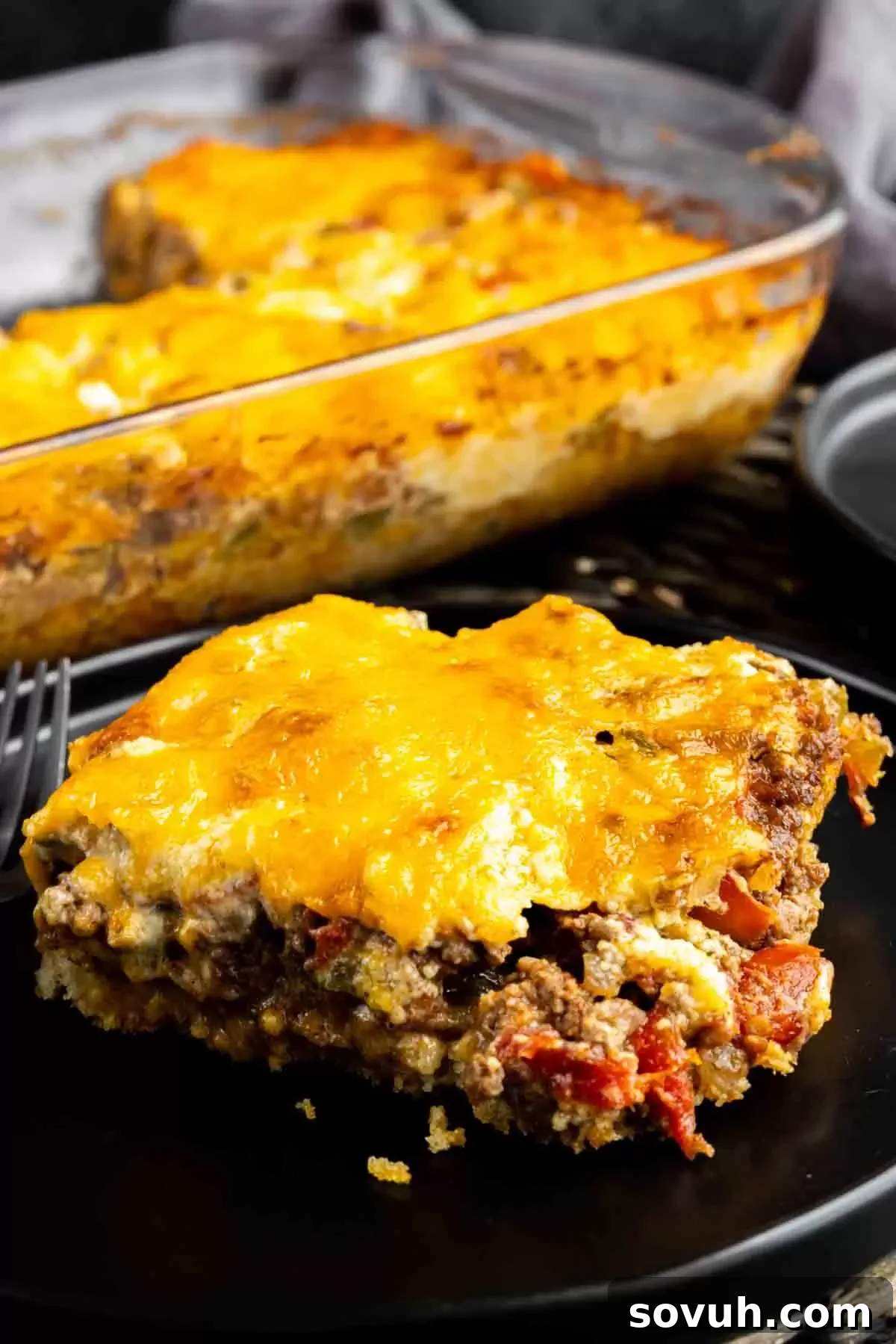 A perfectly baked slice of John Wayne Casserole on a black plate, ready to be enjoyed.